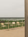 An outdoor patio with ivory Nook Dining Tables, Co Dining Chairs, and an olive Ray Table Lamp, set against a windy sea.