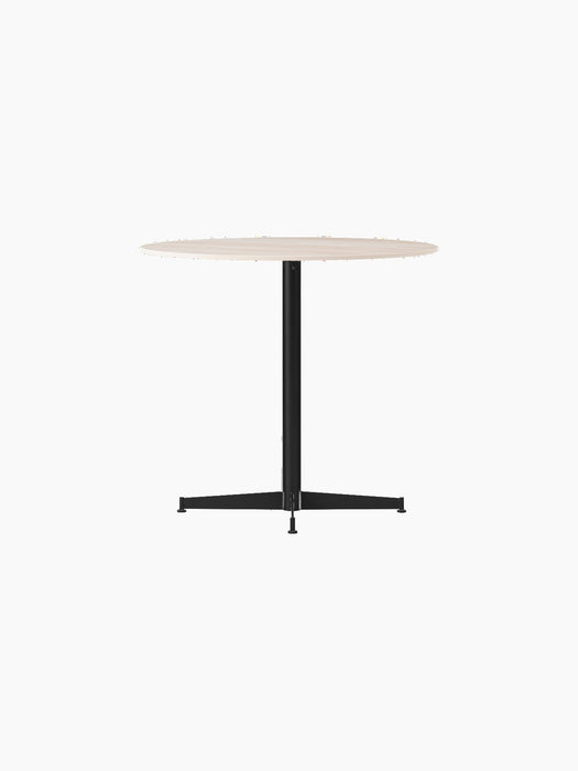Angle view of the Nook Dining Table, featuring a round, light-coloured tabletop and a slim, black four-star pedestal base.