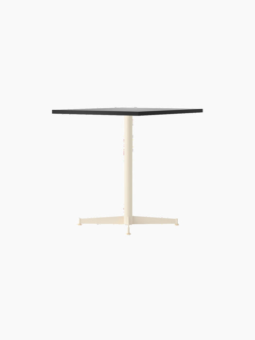Angled view of the Nook Dining Table with a square charcoal linoleum top and a slim, ivory-coloured, four-star steel base.