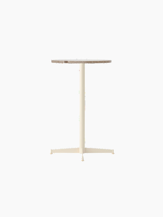 The Nook Counter Table shown at an angle, featuring a round Kunis Breccia stone top and a slim, ivory-coloured metal base.