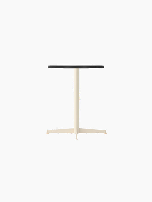 The Nook Dining Table, shown at an angle, featuring a circular black oak veneer top and a slim, four-star base in ivory.