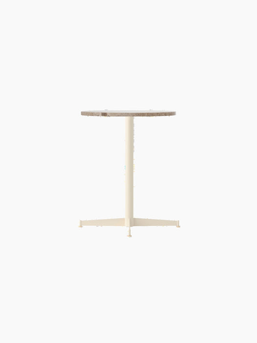 An angled view of the Nook Dining Table with a round Kunis Breccia stone top and a slim, four-star base in ivory.
