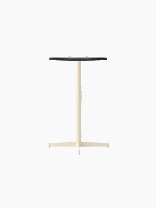 The Nook Counter Table with a round black oak top and an ivory pedestal base with four feet, viewed from an angle.