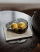 A close-up of the Aer Bowl in smoked glass, holding two yellow quinces. The bowl rests on a book on top of a dark wood table.