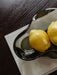 A close-up of the organically shaped Aer Bowl in smoked glass, holding two yellow lemons on a grey book over a dark table.