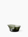An angled view of the Aer Bowl, a sculptural piece of dark, smoky green glass with an organic, undulating rim.