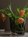 A close-up of the dark smoked glass Aer Vase, filled with a bouquet of orange ruffled tulips, sitting on a marble surface.