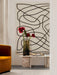 Interior scene with a mustard velvet chair and low marble table with a vase of red flowers before a large abstract painting.