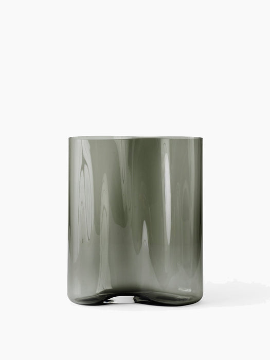 Back view of the small Aer Vase, a cylindrical smoky grey glass vase with a rippled texture and an irregular, footed base.
