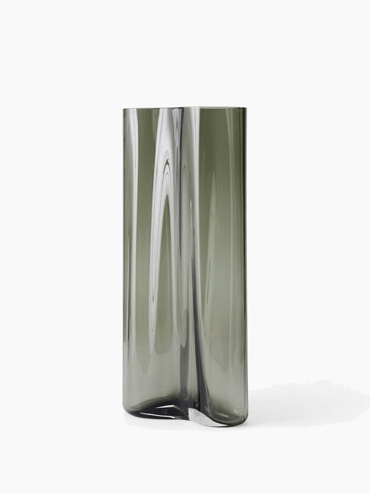 An angled view of the large Aer Vase. The tall, sculptural form is crafted from smoky grey glass with a rippling effect.