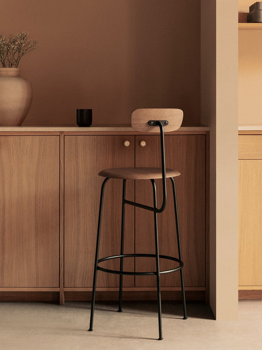 A side-rear view of the Afteroom Bar Chair, Veneer with a black frame, styled in a minimalist kitchen with wooden cabinets.