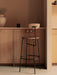 A side-rear view of the Afteroom Bar Chair, Veneer with a black frame, styled in a minimalist kitchen with wooden cabinets.