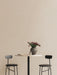 Two black Afteroom Bar Chairs flank a marble-topped Harbour Column Bar Table holding a vase of flowers against a beige wall.