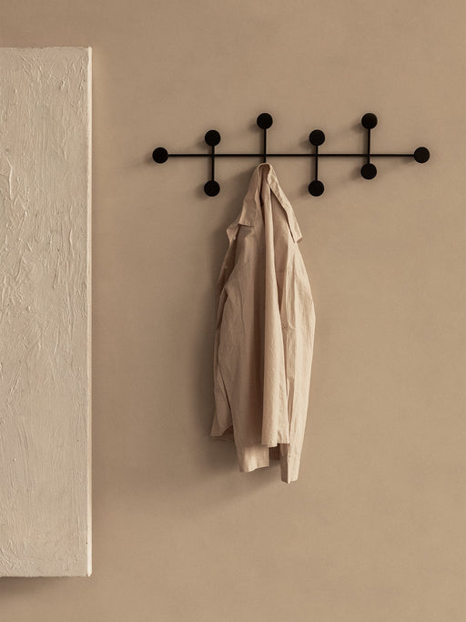 The black Afteroom Coat Hanger Large mounted on a beige wall, with a beige linen shirt hanging from one of the central hooks.