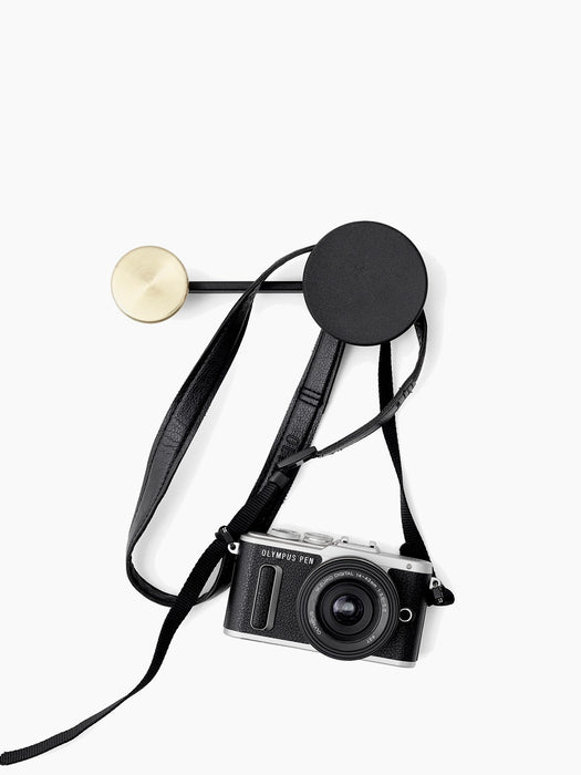 A small Afteroom Coat Hanger in black and brass, with a black and silver Olympus camera hanging by its strap from the hook.