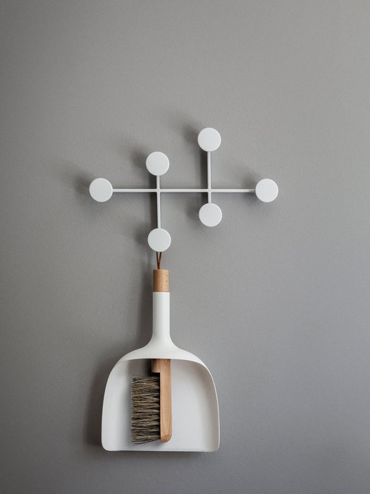 The white Sweeper & Funnel dustpan and brush hangs from the white Afteroom Coat Hanger against a simple grey wall.