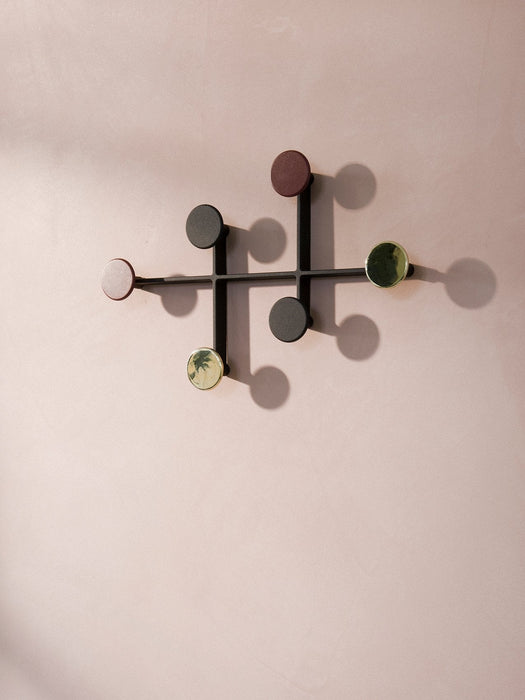 A minimalist black metal Afteroom Coat Hanger with round hooks in multiple colors, fixed to a pale pink, textured wall.