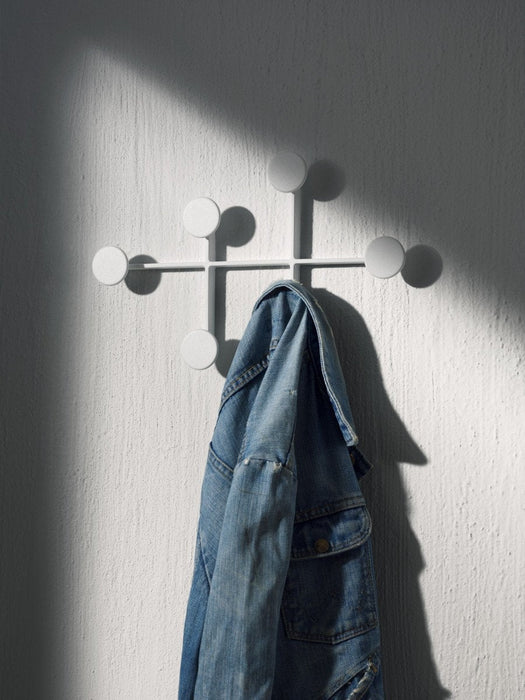 A blue denim jacket hangs on a white Afteroom Coat Hanger, which is mounted on a textured white wall with dramatic shadows.