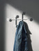 A blue denim jacket hangs on a white Afteroom Coat Hanger, which is mounted on a textured white wall with dramatic shadows.