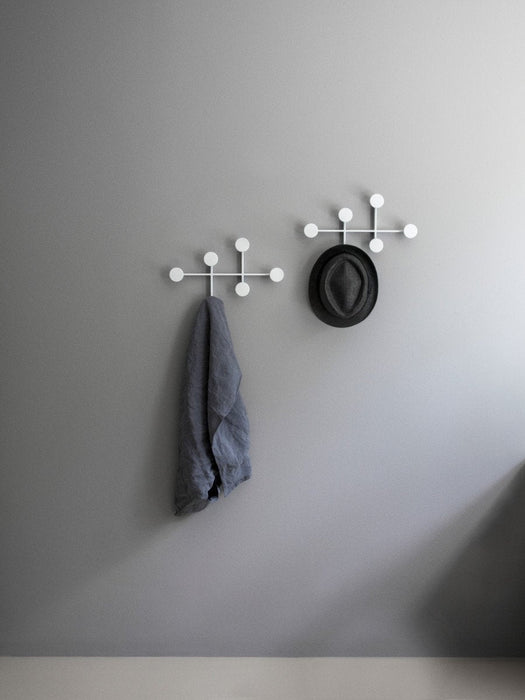 Two white Afteroom Coat Hangers mounted on a grey wall. A grey cloth hangs from one, and a black fedora hat from the other.