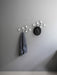 Two white Afteroom Coat Hangers mounted on a grey wall. A grey cloth hangs from one, and a black fedora hat from the other.