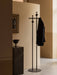 A black Afteroom Coat Stand with a jacket, styled in a hallway next to a tall black marble Plinth with a Pavot Bowl.