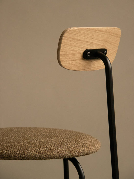 A close-up of the Afteroom Dining Chair, highlighting the natural oak backrest, black steel frame, and textured bouclé seat.