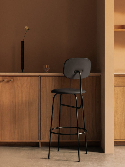 A black Afteroom Bar Chair Plus in a kitchen. On the wooden counter behind is a tall black Stance Vase with a white flower.