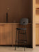 A black Afteroom Bar Chair Plus in a kitchen. On the wooden counter behind is a tall black Stance Vase with a white flower.