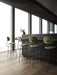 Four green upholstered Afteroom Bar Chair Plus at a dark bar in a modern room with large windows and light wood floors.