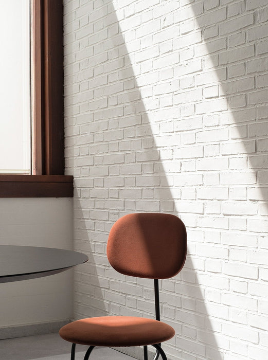 The terracotta Afteroom Dining Chair Plus, set against a white brick wall, is partially lit by a strong ray of sunlight.