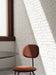 The terracotta Afteroom Dining Chair Plus, set against a white brick wall, is partially lit by a strong ray of sunlight.