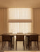 A long dark wood Androgyne Dining Table with matching Ready Dining Chairs, illuminated by a Hashira Linear Pendant Lamp.