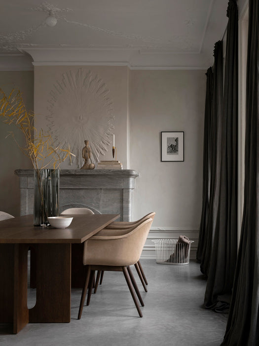 A dark Androgyne Dining Table and beige Harbour Dining Chairs in a room with a fireplace, Aer Vase and white Ribbon Basket.