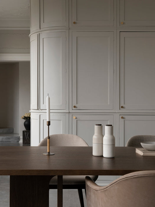 A dark oak Androgyne Dining Table featuring a Duca Candle Holder and Bottle Grinders, with beige Harbour Chairs.