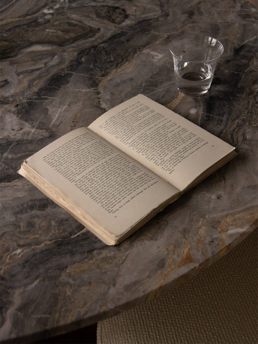 A close-up, overhead shot of the Androgyne Dining Table's Grey Galaxy marble top with an open book and a glass of water.