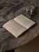 A close-up, overhead shot of the Androgyne Dining Table's Grey Galaxy marble top with an open book and a glass of water.
