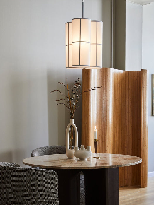 A round Androgyne Dining Table with a marble top and dark base, styled with vases and a candle, under a lit Hashira lamp.