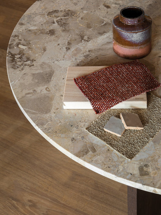 A close-up of the Androgyne Dining Table's Kunis Breccia stone top, featuring a ceramic vase and various material swatches.