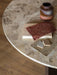 A close-up of the Androgyne Dining Table's Kunis Breccia stone top, featuring a ceramic vase and various material swatches.