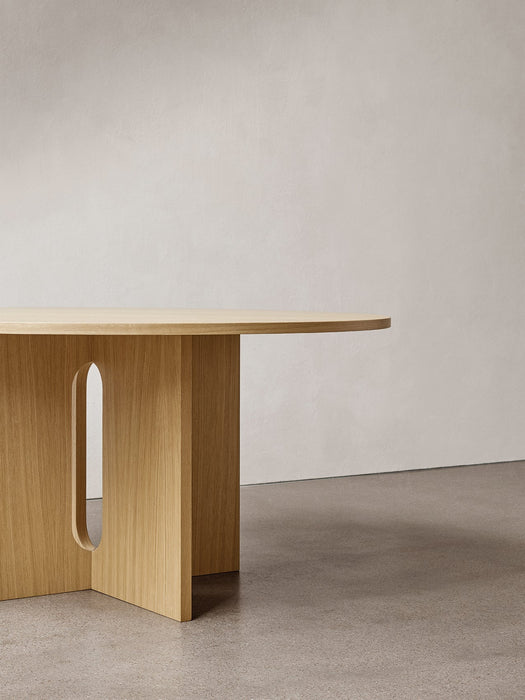 Close-up of the Androgyne Dining Table in natural oak, focusing on the sculptural base with its distinctive arched cut-out.