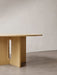 Close-up of the Androgyne Dining Table in natural oak, focusing on the sculptural base with its distinctive arched cut-out.