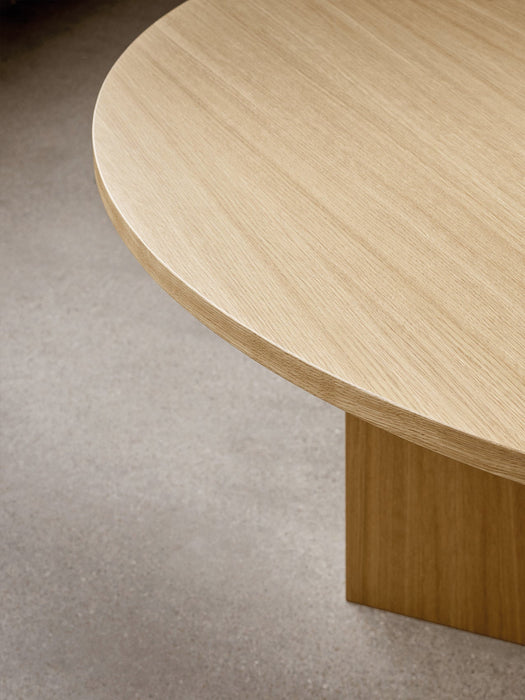 A close-up shot of the round Androgyne Dining Table in natural oak, highlighting the wood grain of the tabletop and base.