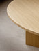 A close-up shot of the round Androgyne Dining Table in natural oak, highlighting the wood grain of the tabletop and base.