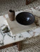 Close-up of the Androgyne Lounge Table with a marble top and wood base, styled with a book, vase, and bowl on a textured rug.