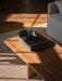 A dark wood Androgyne Lounge Table sits on a striped rug, styled with a book and decorative bowl in a sunlit room.