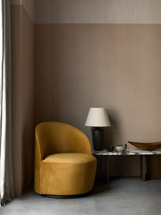 A Tearoom Lounge Chair in yellow velvet beside a marble Androgyne Lounge Table, styled with a black Torso Table Lamp.