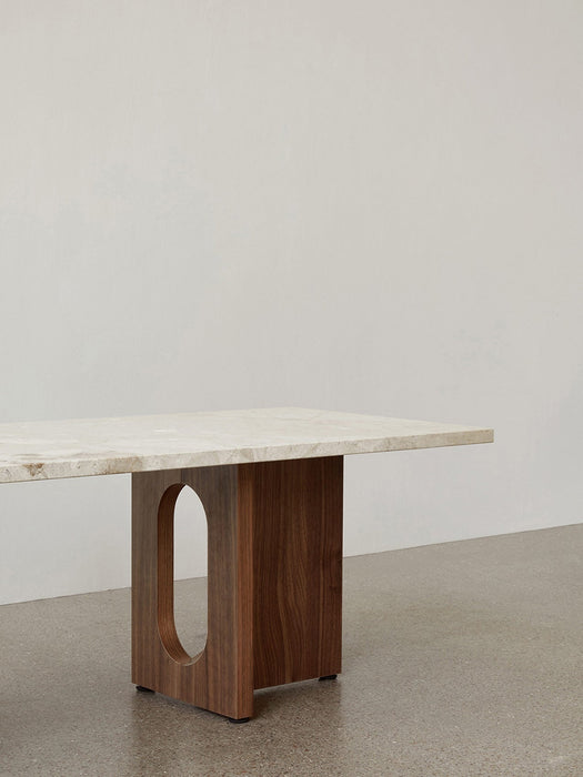 A side-profile close-up of the Androgyne Lounge Table, featuring a light stone top and a dark wood base with an oval cutout.