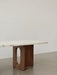 A side-profile close-up of the Androgyne Lounge Table, featuring a light stone top and a dark wood base with an oval cutout.