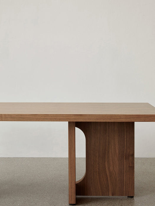 A close-up of the Androgyne Lounge Table in walnut, highlighting the smooth wooden tabletop and the arched leg design.
